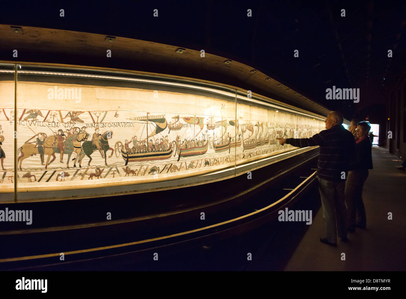 A couple of tourists admiring the Bayeux tapestry or La Tapisserie de la Reine Mathilde in it's current display case Stock Photo