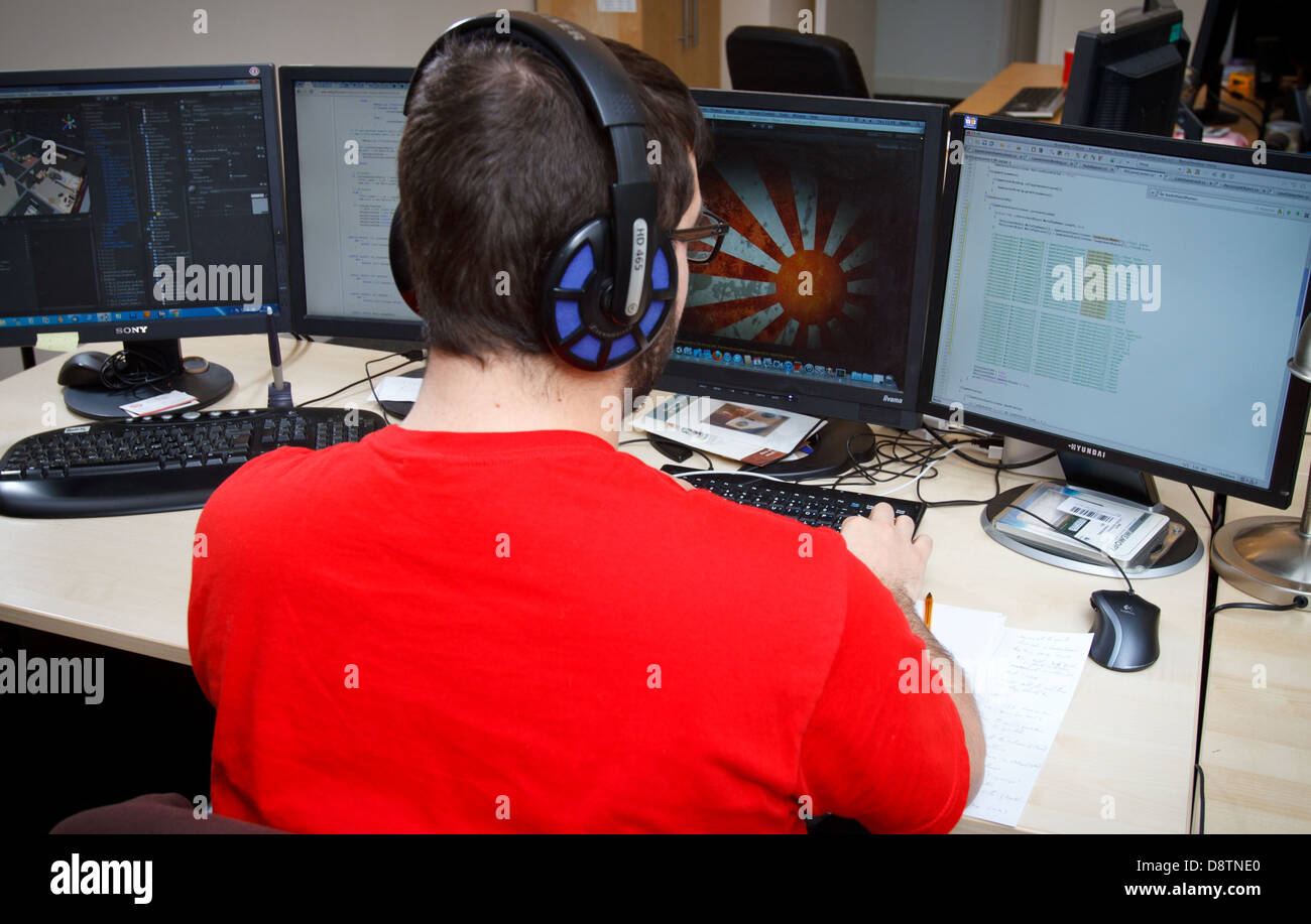 A graphic designer works at his desk infront of several large monitors. Stock Photo