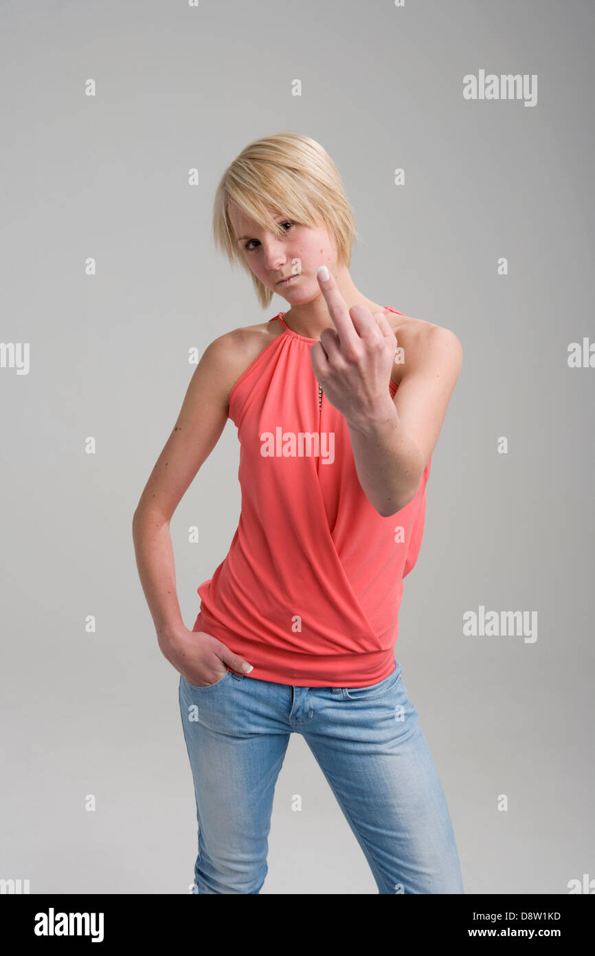 Blonde young woman (20) in studio blue jeans and pink top, making one-finger gesture at camera Stock Photo