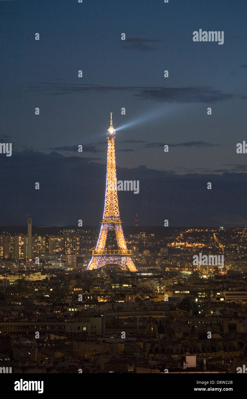 Eiffel Tower lit up at night, with rotating searchlight on top, seen