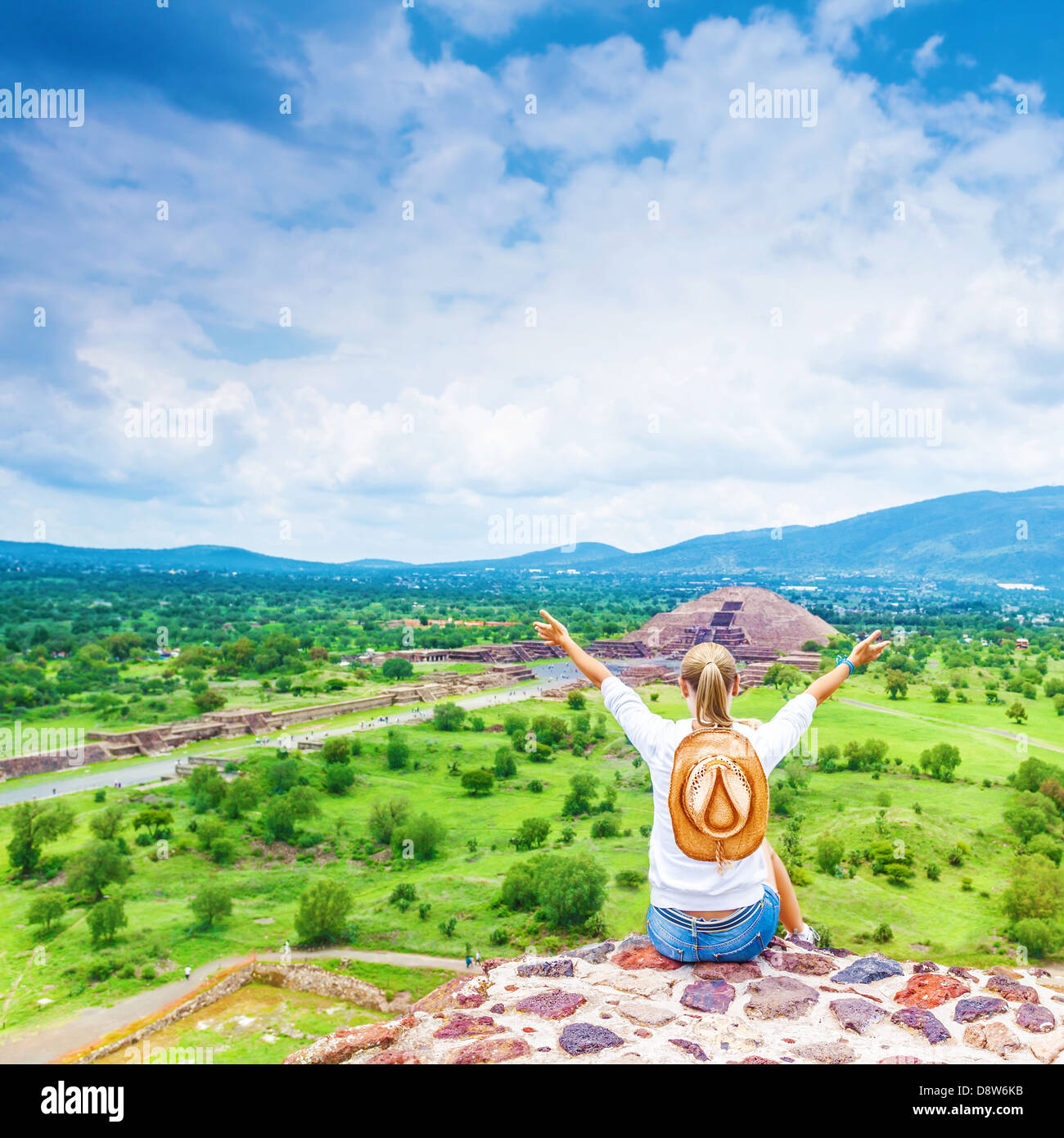 Back side of tourist girl sitting with raised up hands on the top of mountains and enjoying view of Mexican pyramid, active life Stock Photo