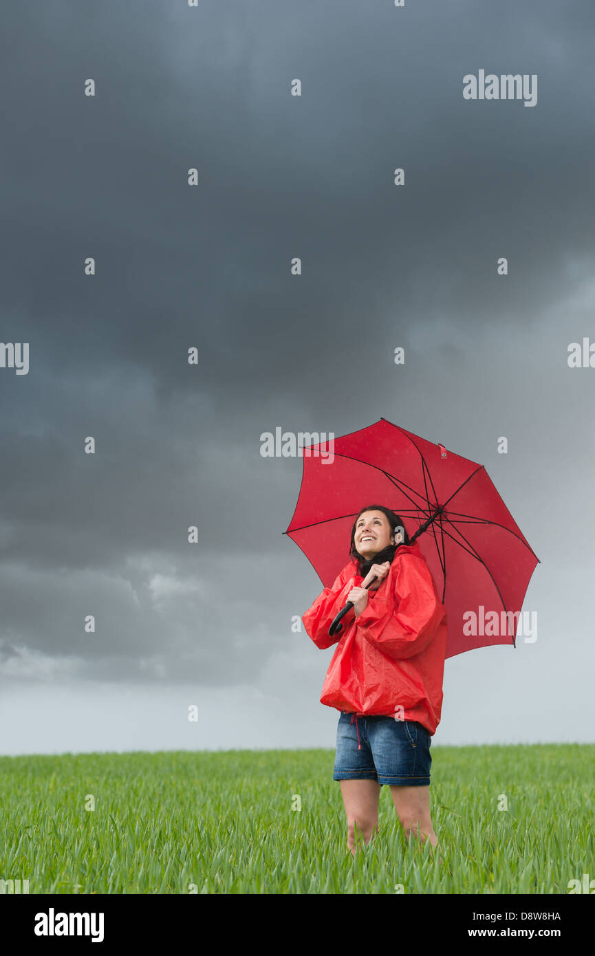 Lively girl daydreaming on rainy day on field with umbrella Stock Photo