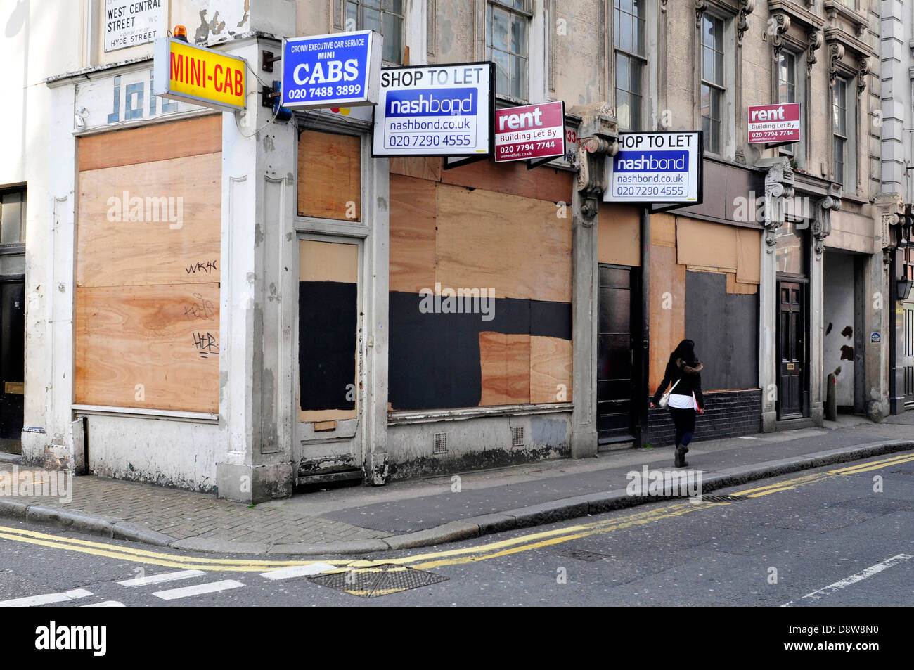 A woman walks past a boarded up shop in central London, UK. Stock Photo