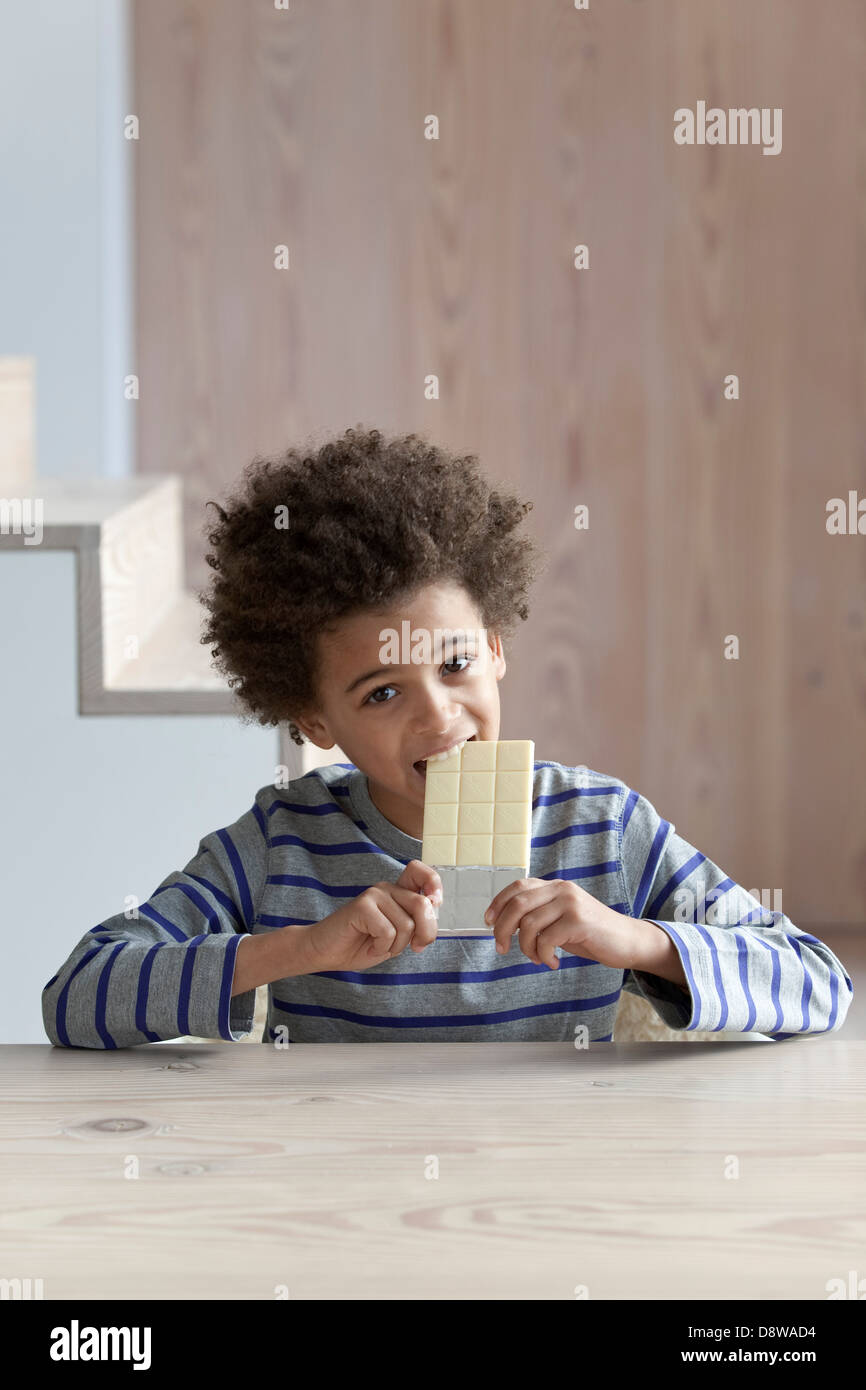 Boy taking a bite out of a bar of white chocolate Stock Photo