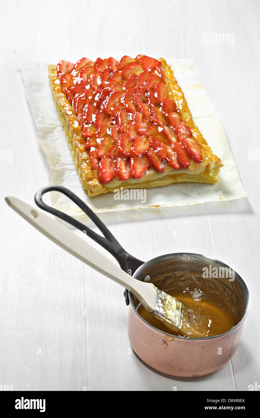 Coating the strawberry tart with heated apricot jam Stock Photo
