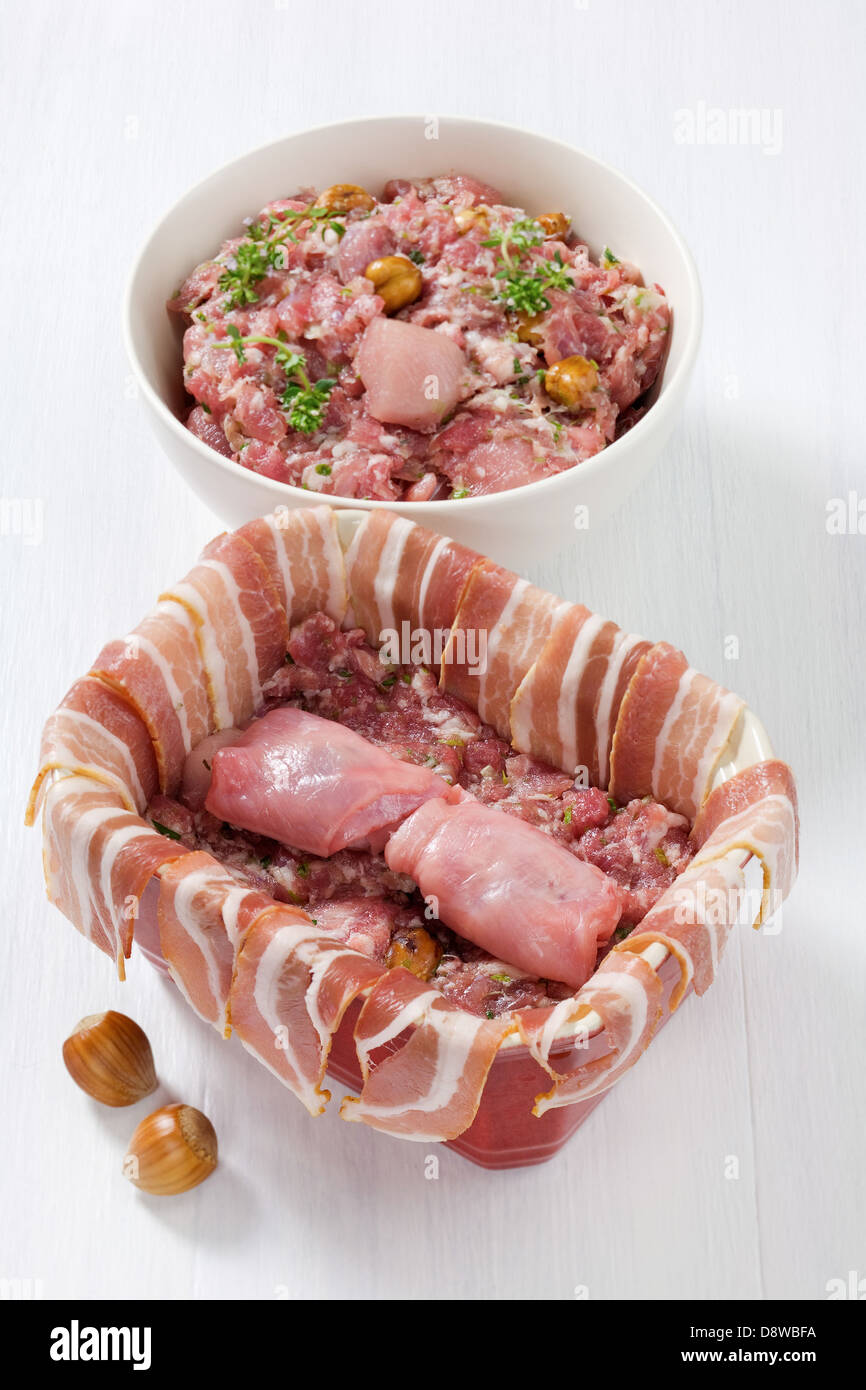 Coating the terrine with steaky bacon and filling the terrine with the rabbit and hazelnut preparation Stock Photo