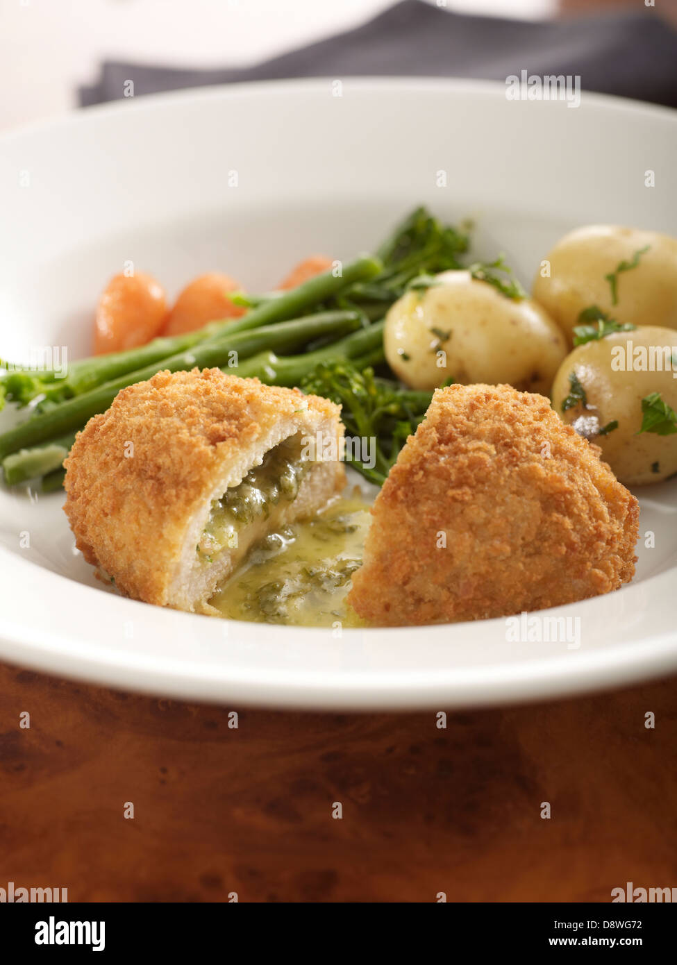 chicken kiev cut open oozing releasing hot butter herbs potatoes green beans carrots Stock Photo