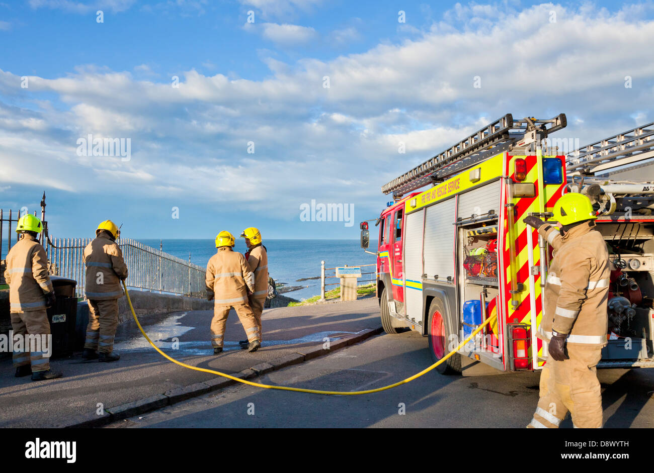 Firemen putting out a small fire in a litter bin at the seaside using a long fire hose from a fire engine Stock Photo