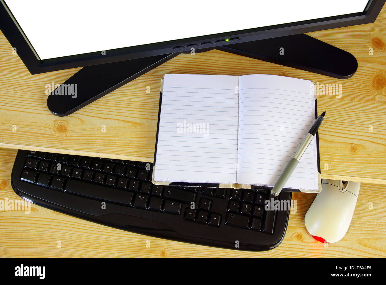 Computer desk with monitor, keyboard, mouse and an opened notebook and pen Stock Photo