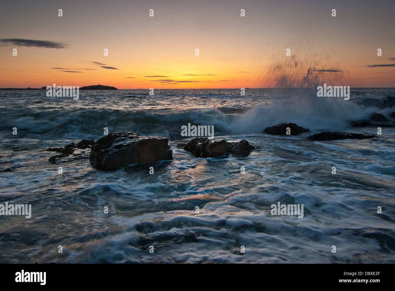 Waves crash and shoot into the air on a rocky beach at sunrise Stock Photo