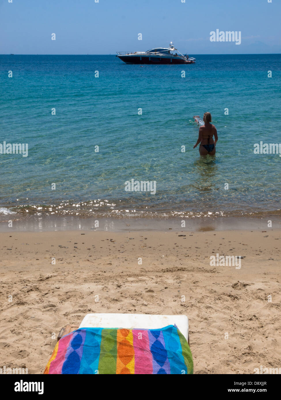 A holidaymaker stands in the Aegean Sea looking out to a motorboat off the Greek island of Skiathos. Stock Photo