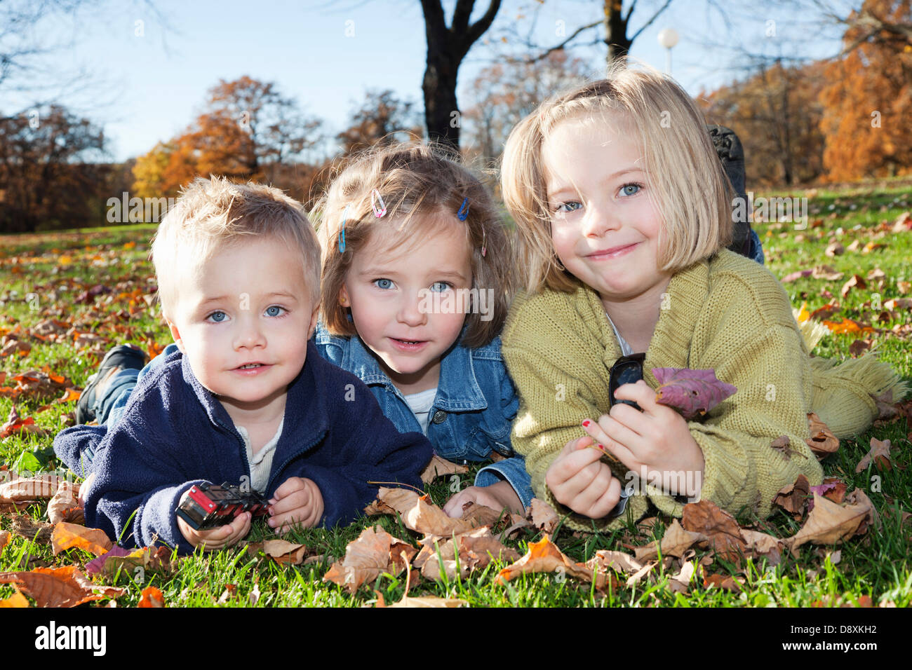 Two year-old boy with his sisters, six and four year-old, in autumn in a park Stock Photo
