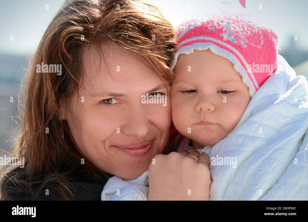 Young European woman holds her sleepy baby girl in blanket Stock Photo