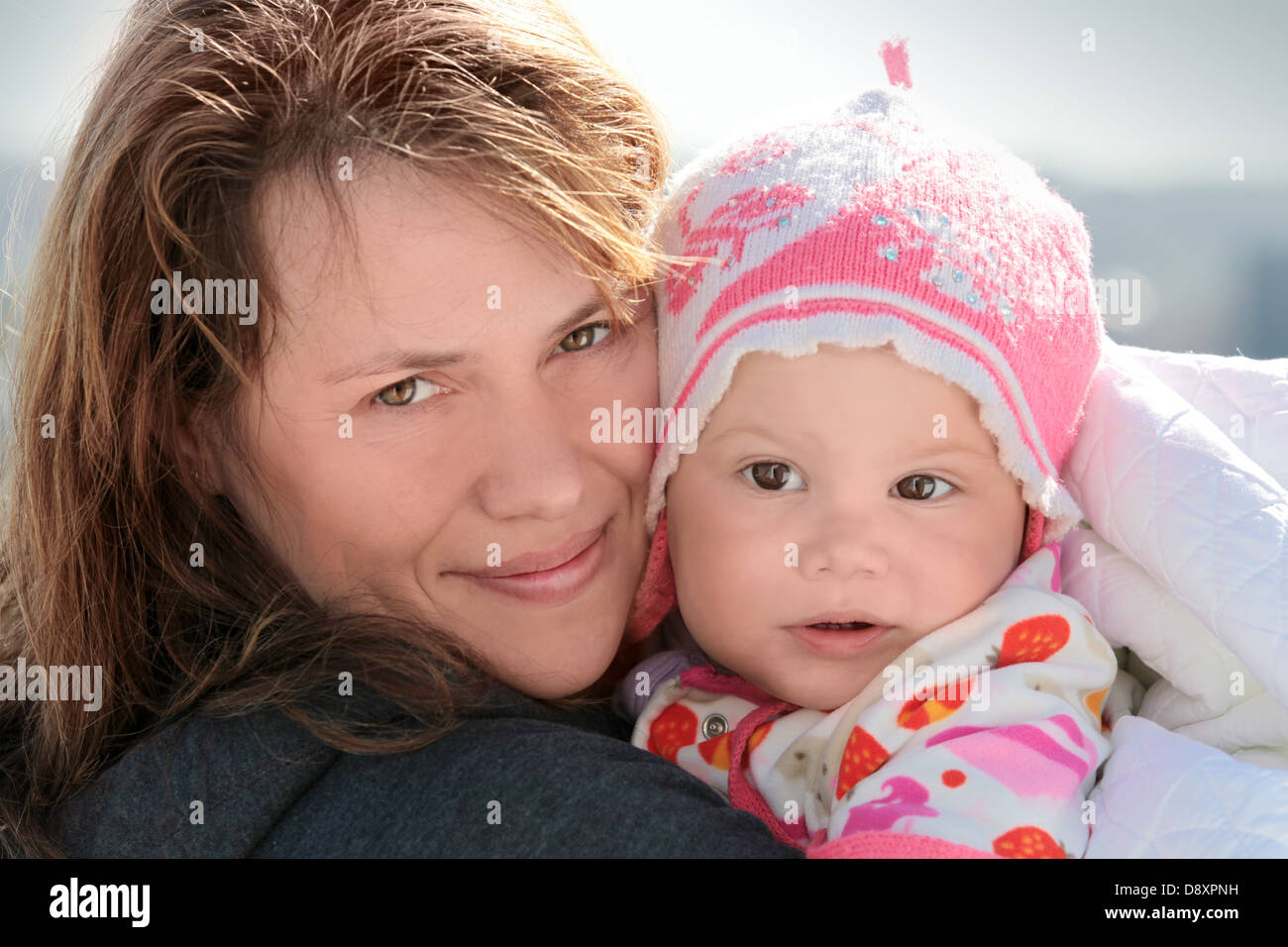 Young woman holds her sleepy baby girl in blanket. Outdoor closeup portrait Stock Photo