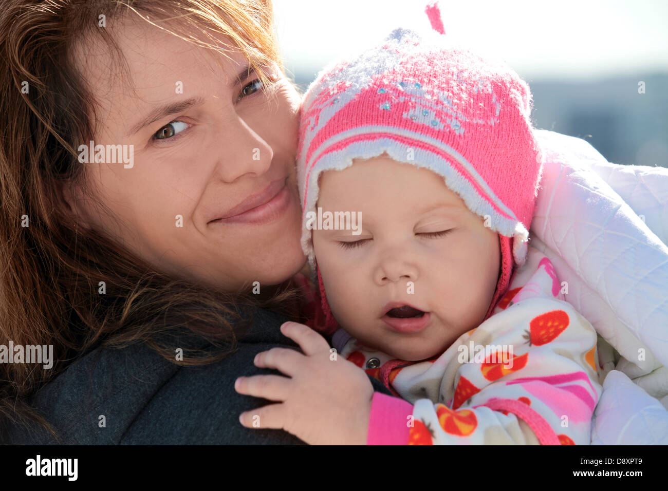 Young European woman holds her sleepy baby girl in blanket. Outdoor closeup portrait Stock Photo