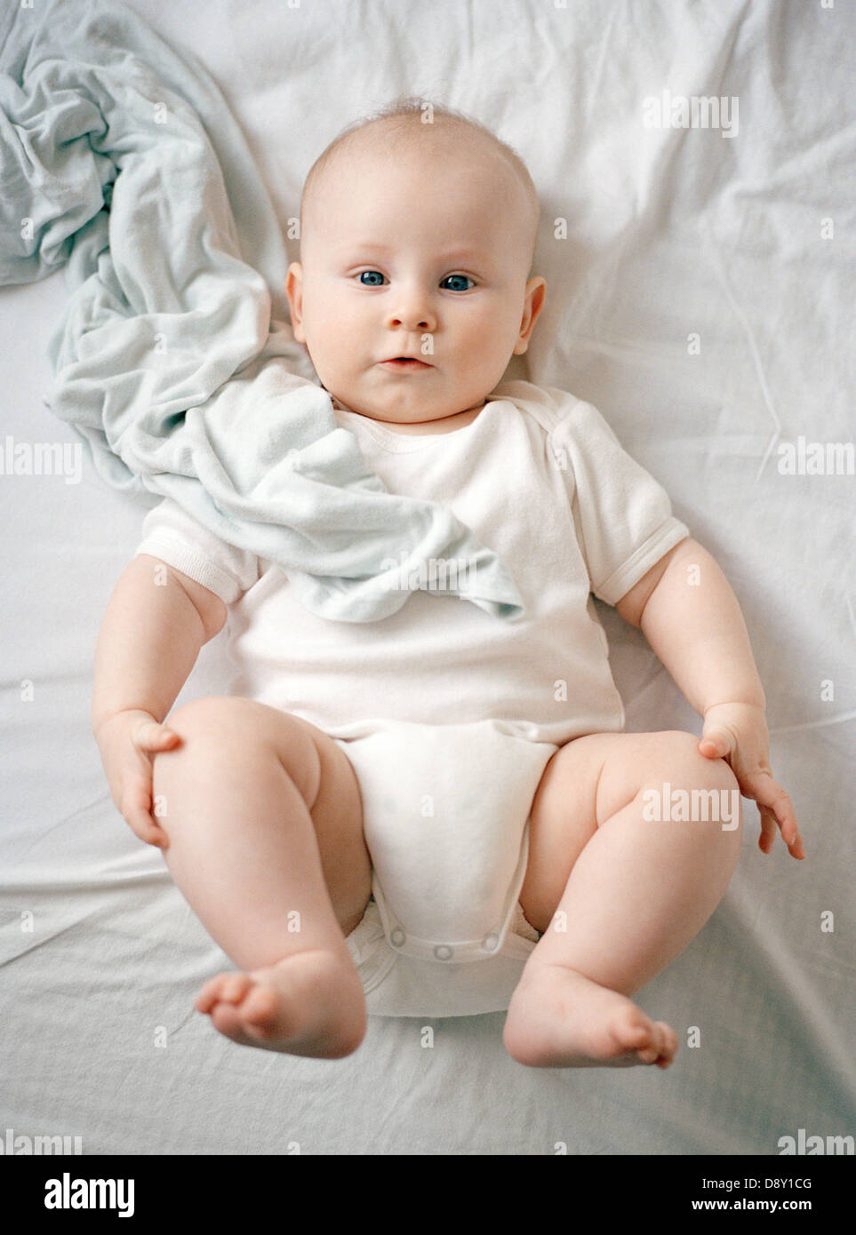 Baby in white clothes lying on whit bed. Stock Photo