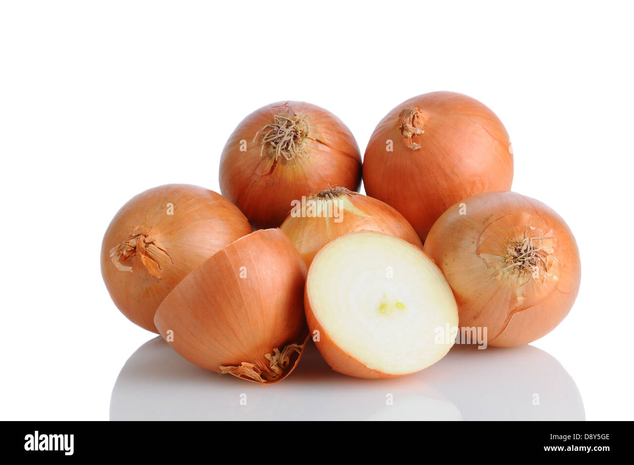 Closeup of a pile of yellow onions on a white surface with reflection. One onion is cut in half, horizontal format. Stock Photo