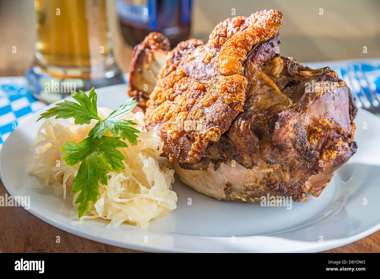 Oktoberfest pork hock with cabbage on a table with beer and Bavarian white blue napkin Stock Photo