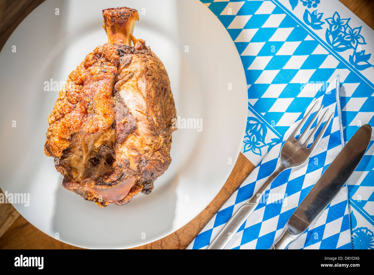 Oktoberfest pork hock on a table with Bavarian white bluw napkin and fork with knife Stock Photo