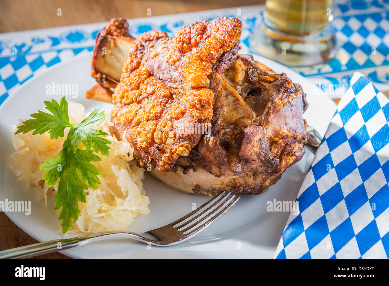 Oktoberfest pork hock with cabbage on a table with beer and Bavarian white blue napkin and fork Stock Photo