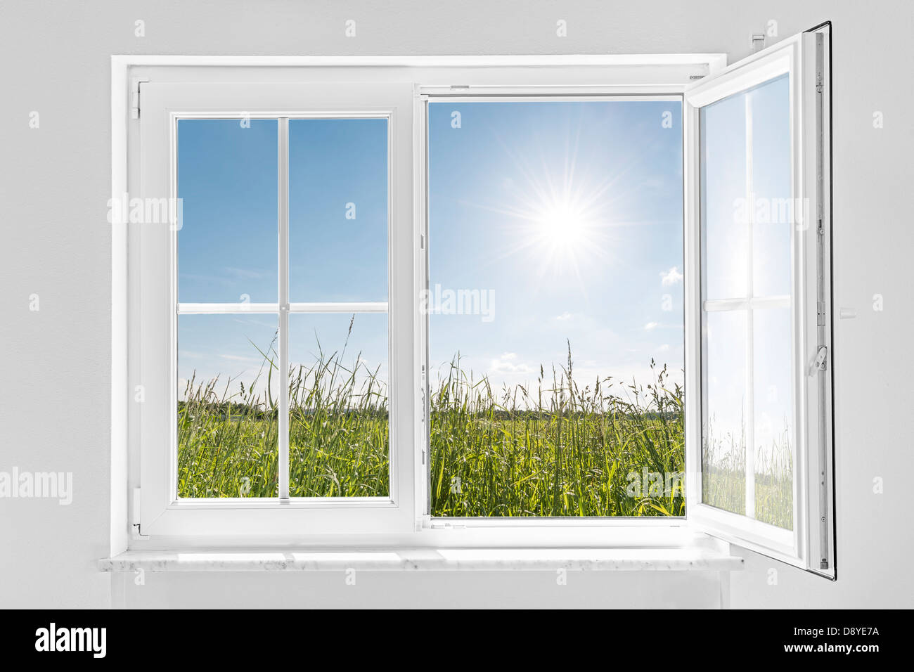 picture of a white wall with white half open window indoor and outside green meadow with sun and blue sky Stock Photo