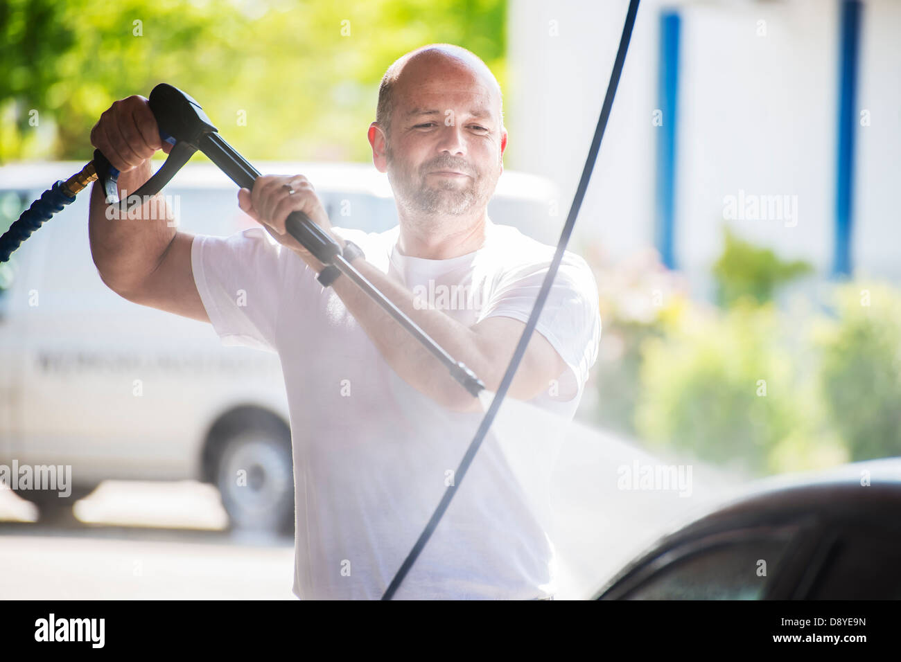 Bald man with a beard is washed with a pressure washer on a sunny day Stock Photo