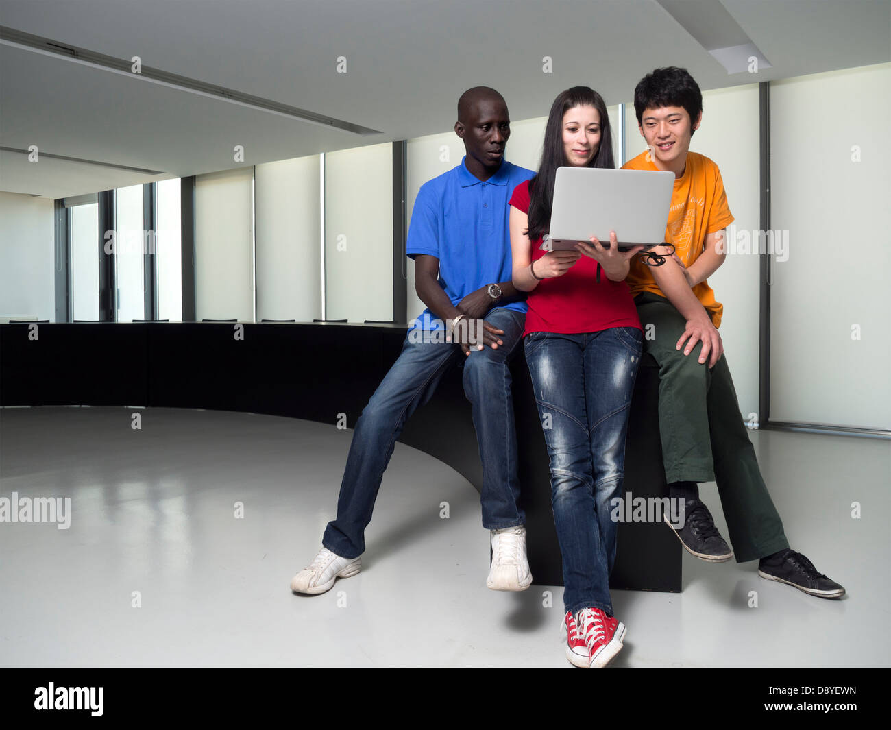 Black man, asian man and caucasian woman gathered around a laptop computer Stock Photo