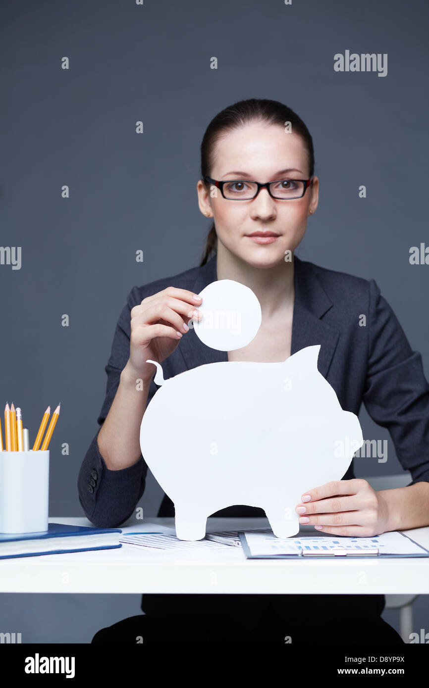 Portrait of young businesswoman with paper piggy bank and coin looking ...