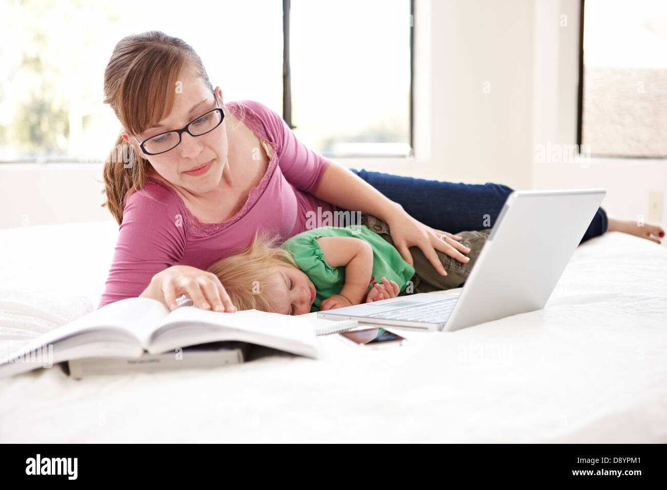 Woman studying on bed with daughter sleeping beside Stock Photo Alamy