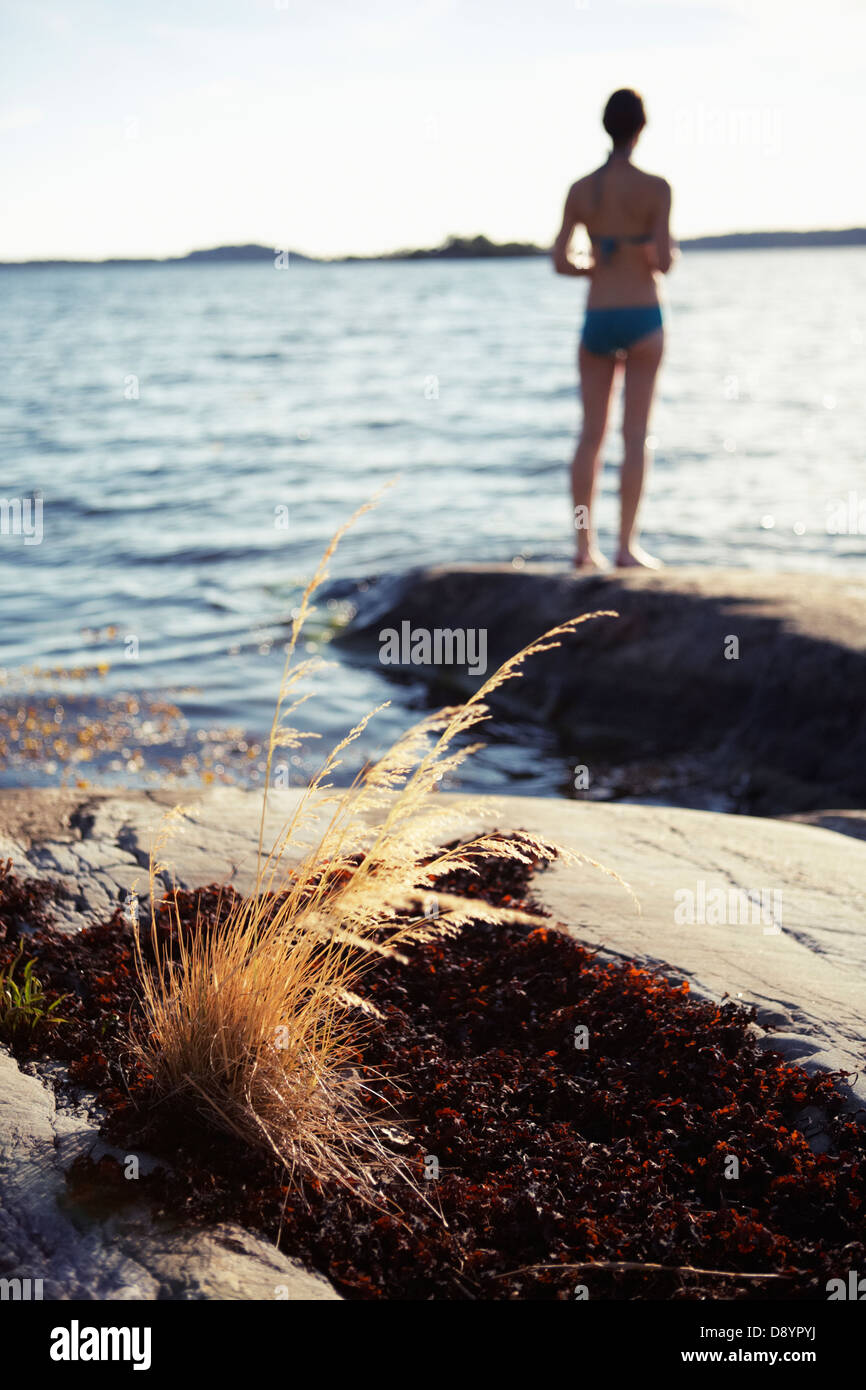 Woman in bikini standing on boulder and looking at sea Stock Photo