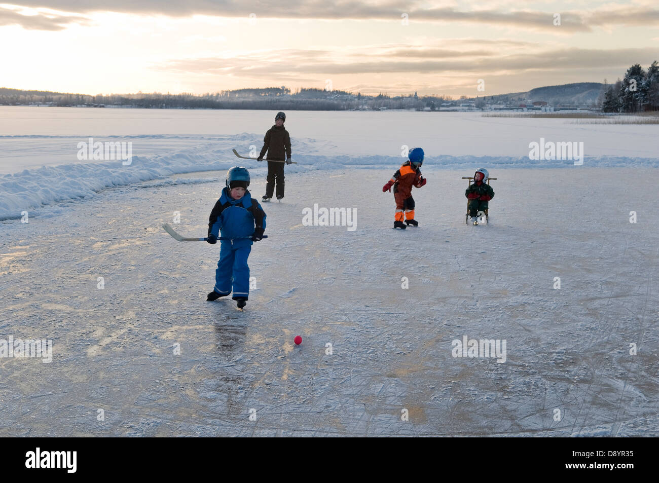 Children playing ice hockey on frozen lake Stock Photo