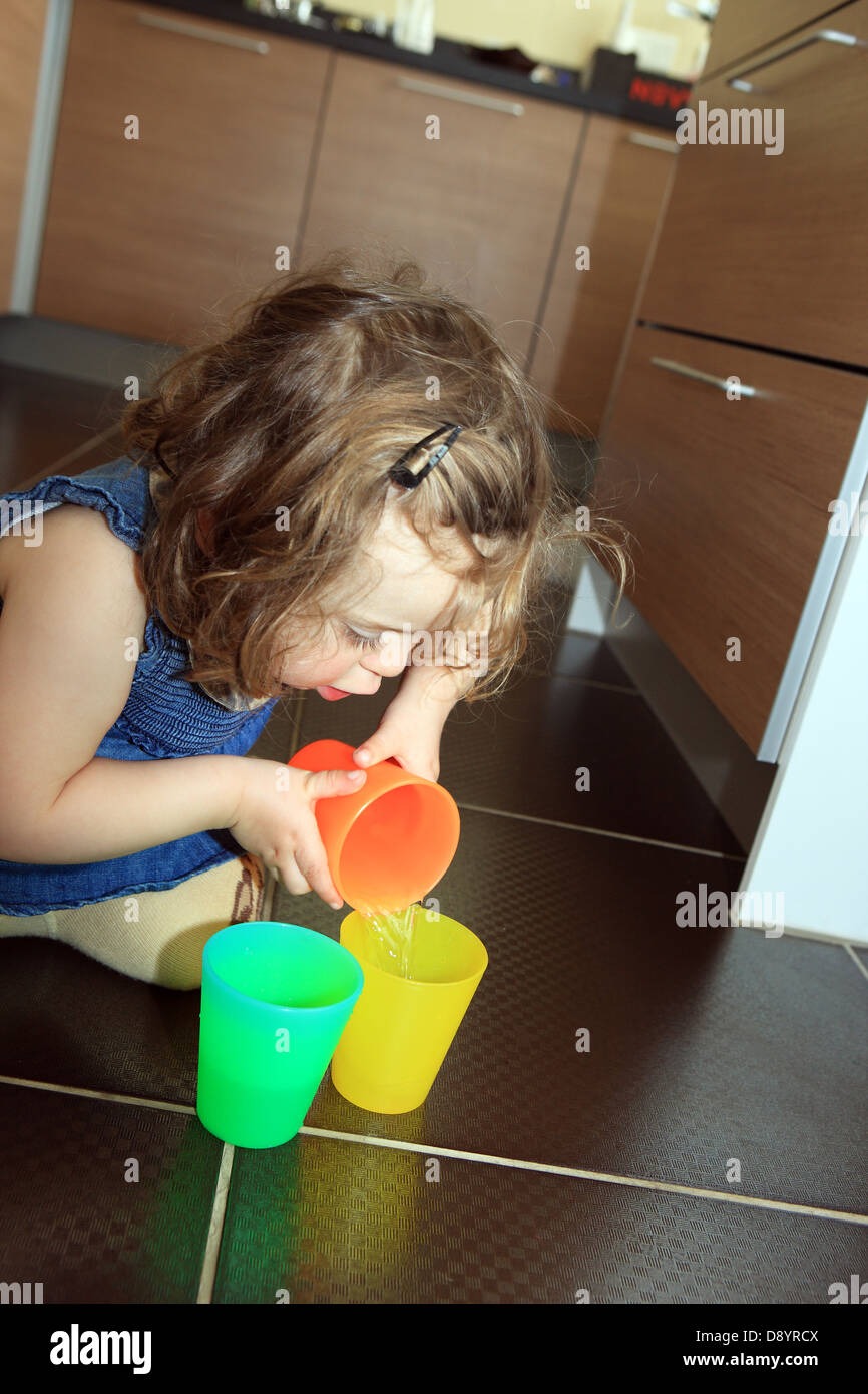 2 year old girl learning and playing water from one coloured tumbler to another Stock Photo