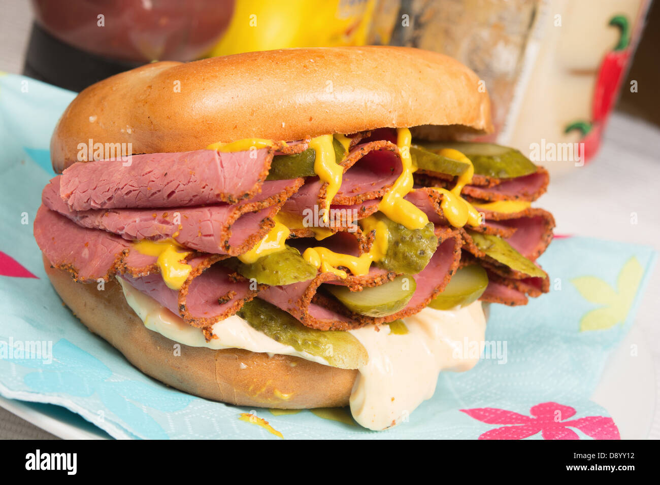 A plain bagel filled with pastrami, sliced gherkins, mustard and chili