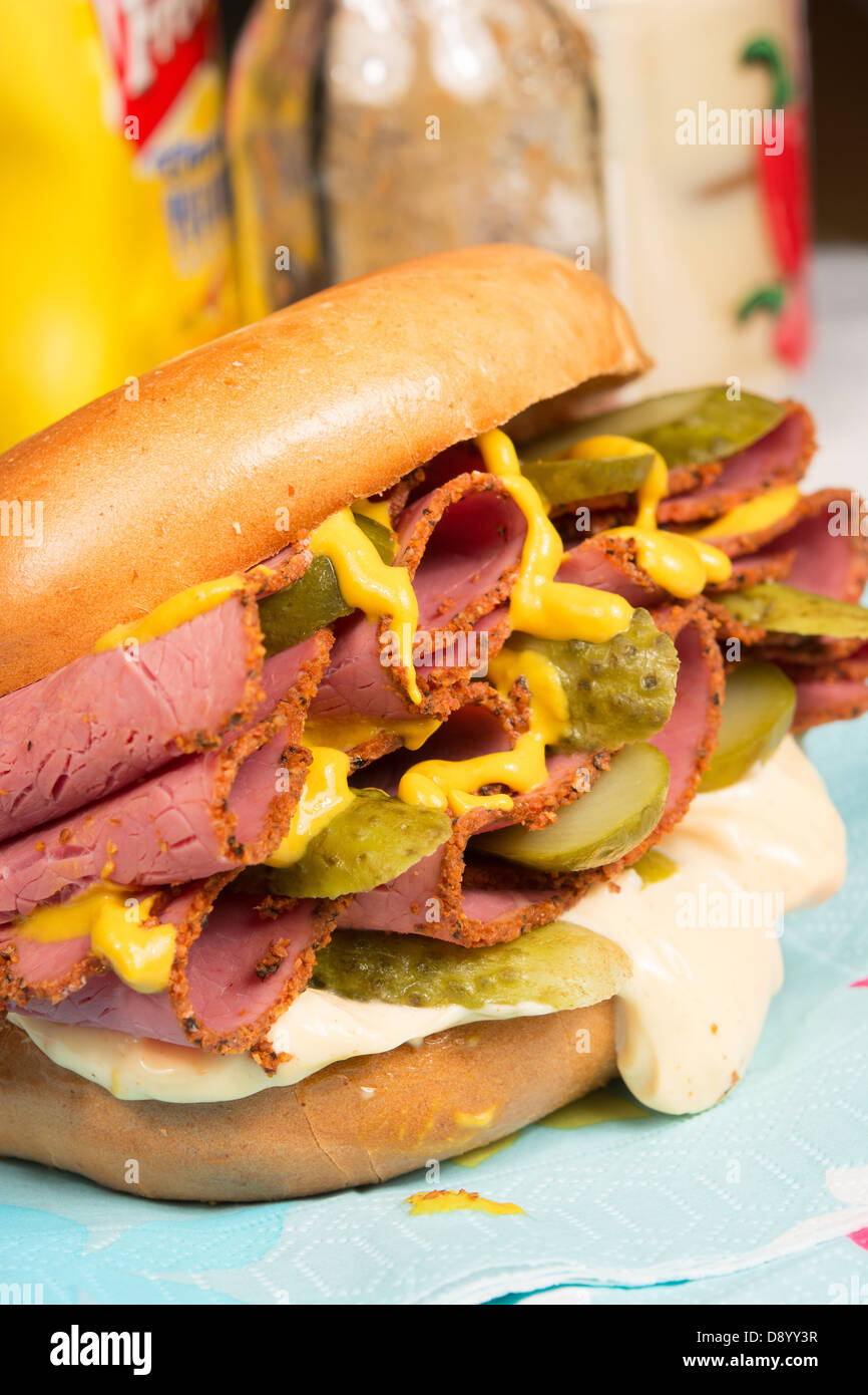 A plain bagel filled with pastrami, sliced gherkins, mustard and chili