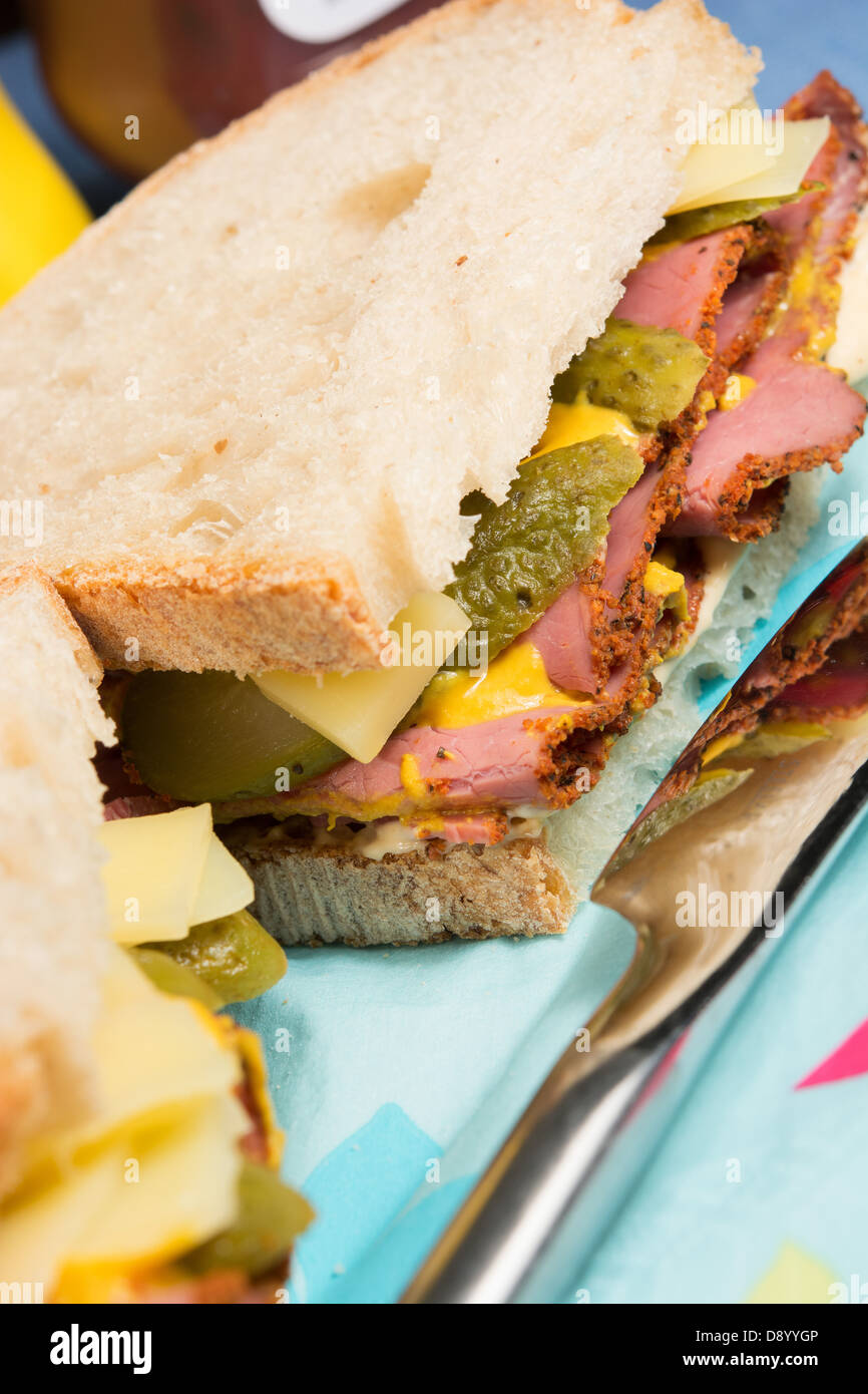 A deli-style sandwich of pastrami, Emmenthal cheese, sliced gherkins, mustard and chili mayonnaise on sourdough bread. Stock Photo