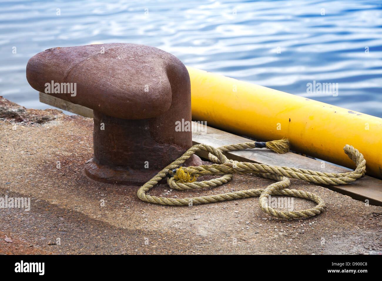 Old rusted mooring bollard with naval rope on concrete pier Stock Photo