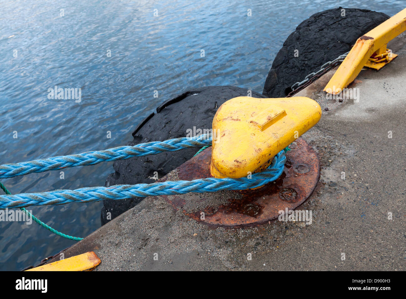 Yellow mooring bollard with blue naval rope on the pier Stock Photo