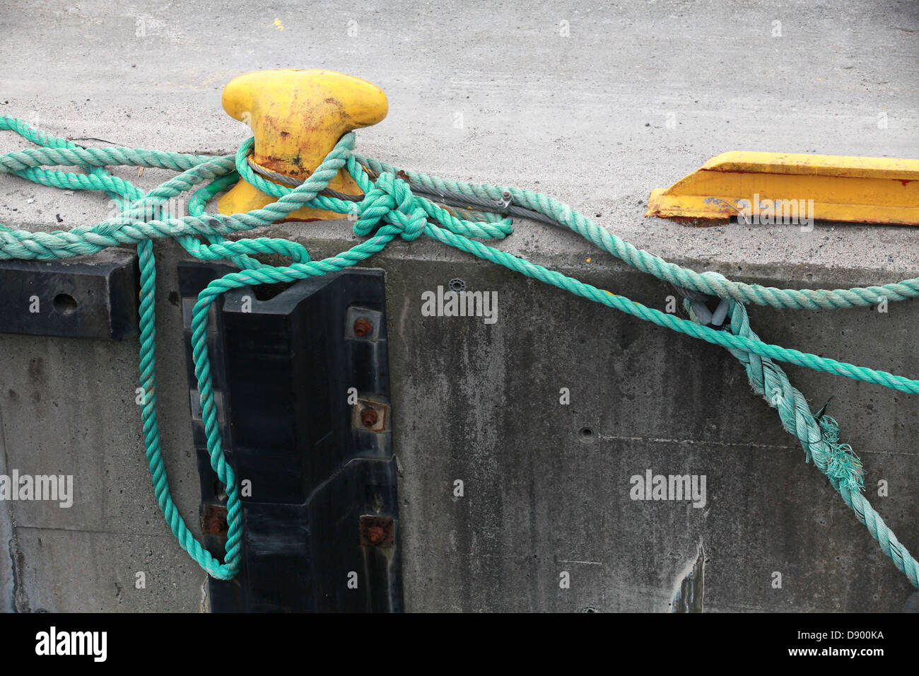 Yellow mooring bollard with green naval rope on the pier Stock Photo