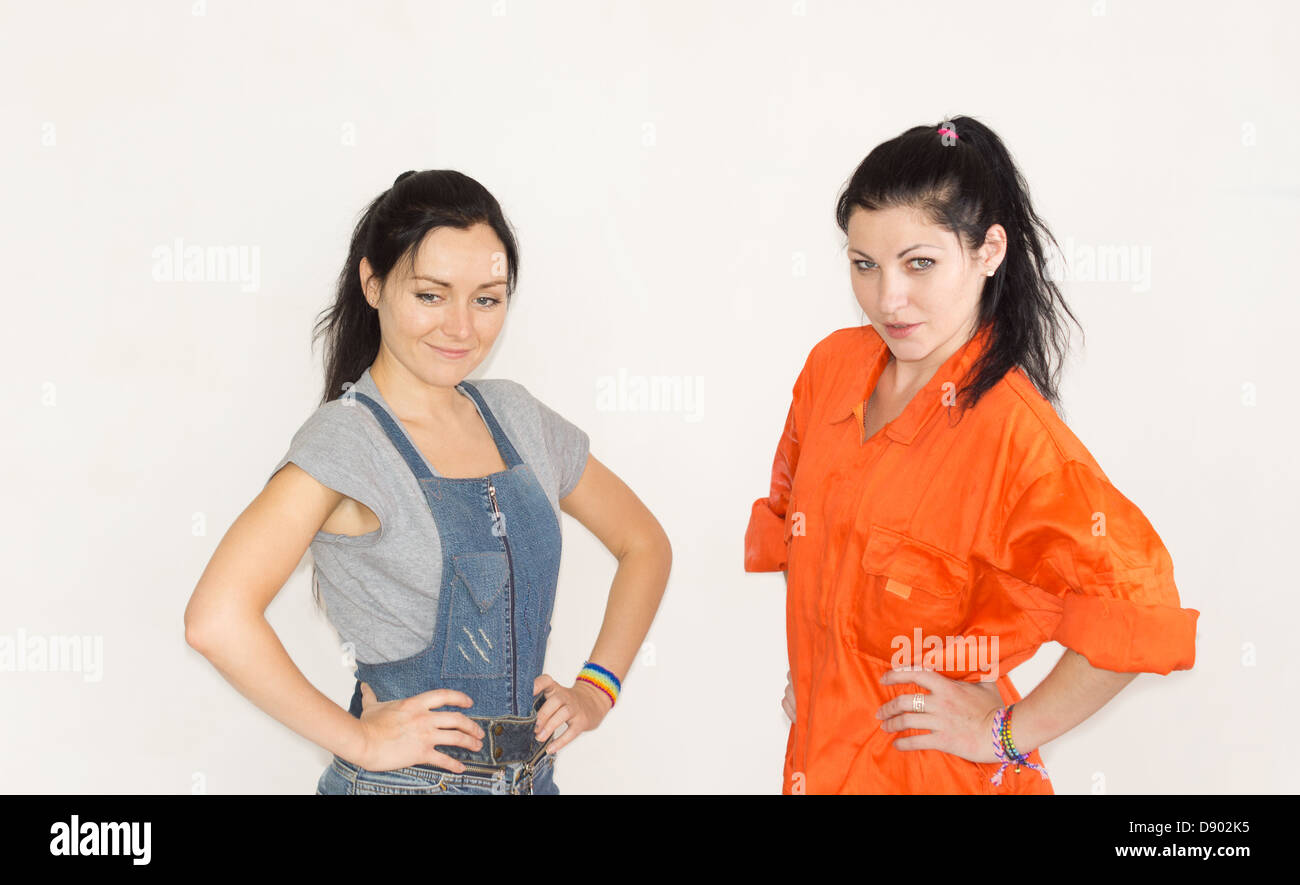 Two capable confident young woman posing in overalls and dungarees with their hands on their hips Stock Photo