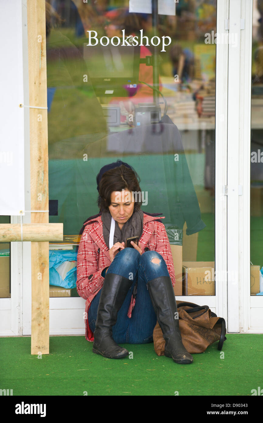 Young woman sat on floor outside bookshop using smart phone at Hay Festival 2013 Hay on Wye Powys Wales UK Stock Photo
