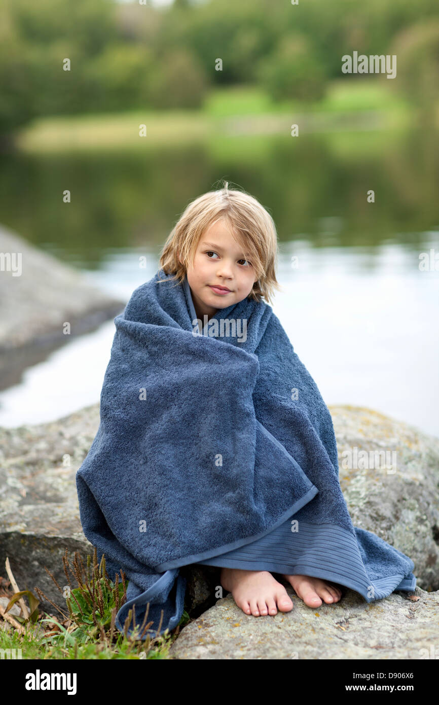 Portrait of boy wrapped in towel sitting by lake Stock Photo