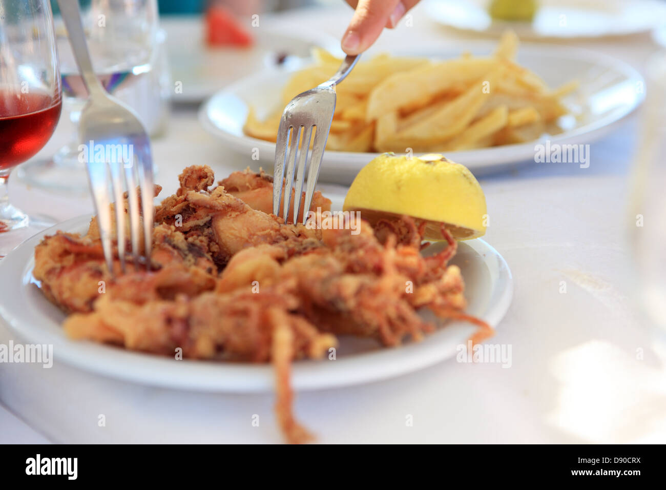 Forks picking up a piece of deep fried squid or Calamari from a plate in a Greek restaurant Stock Photo