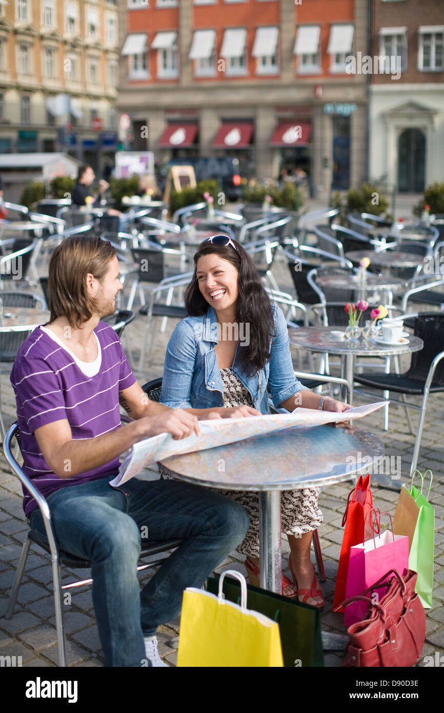 Couple sitting in cafe holding map, laughing Stock Photo