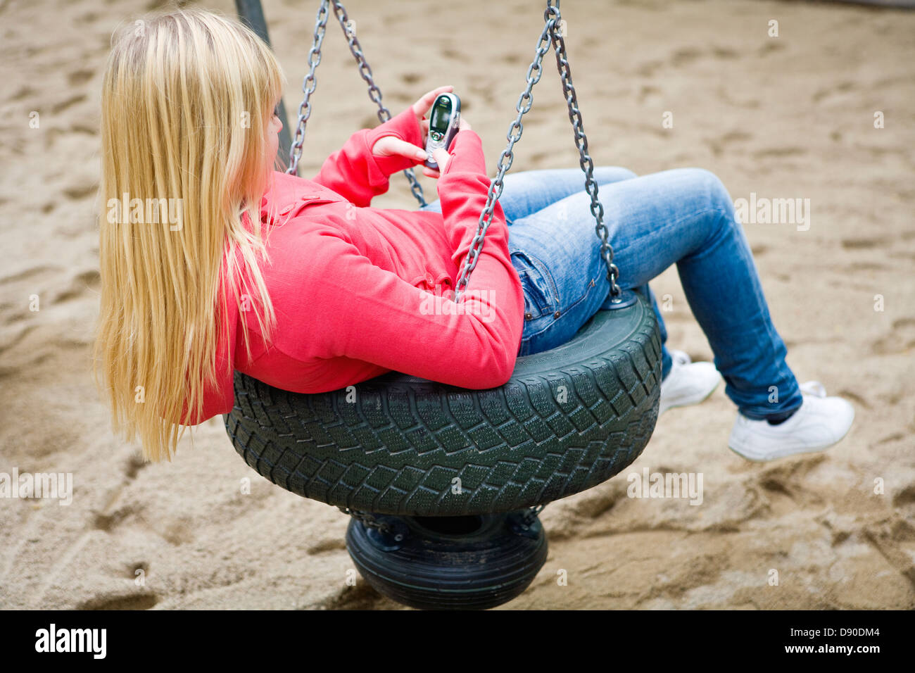 Girl using mobile phone on swing in park Stock Photo