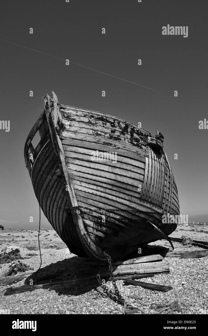 An abandoned wooden boat on a shingle beach in black and white Stock Photo