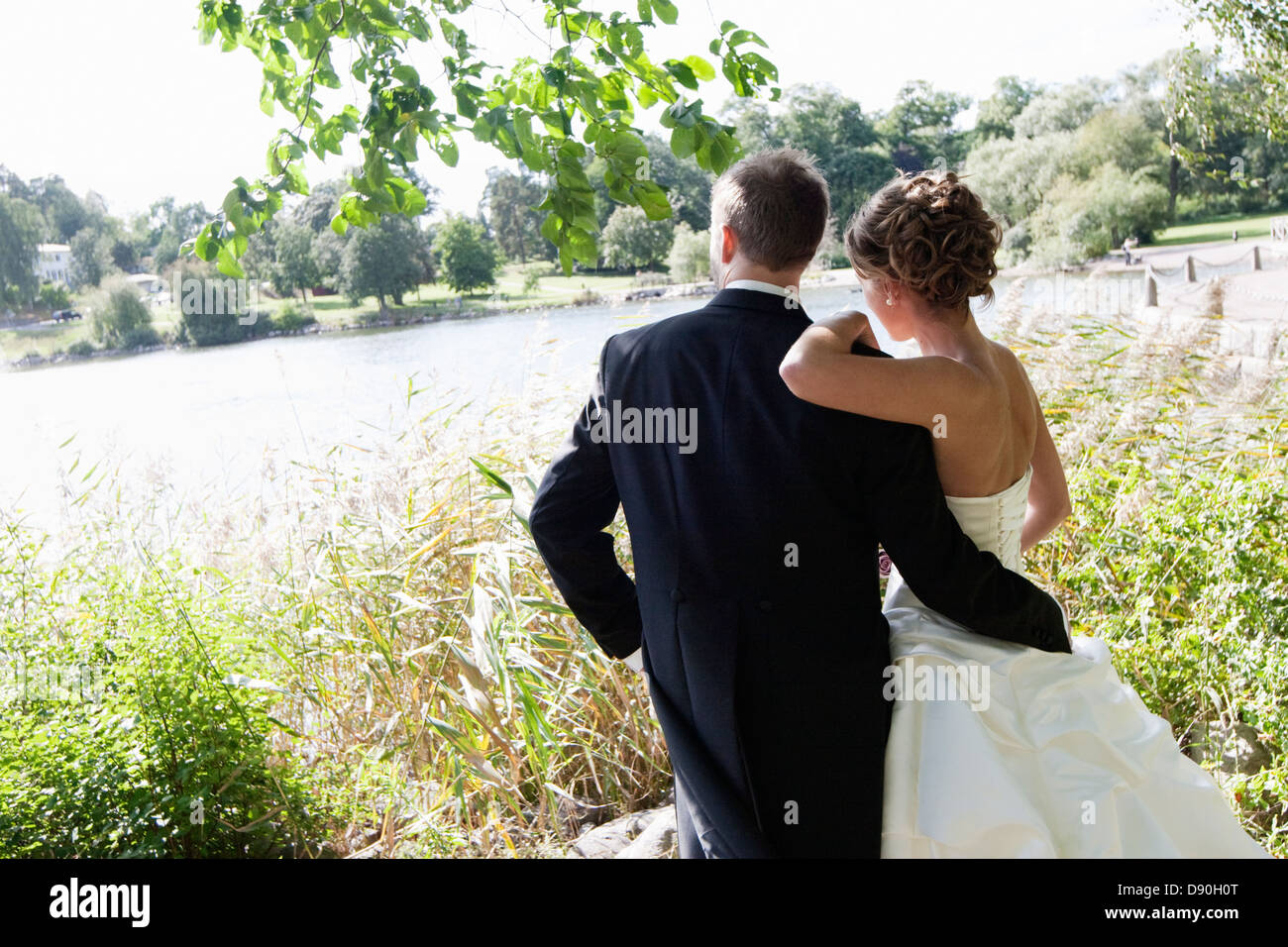 Bridal couple standing near lake at park Stock Photo