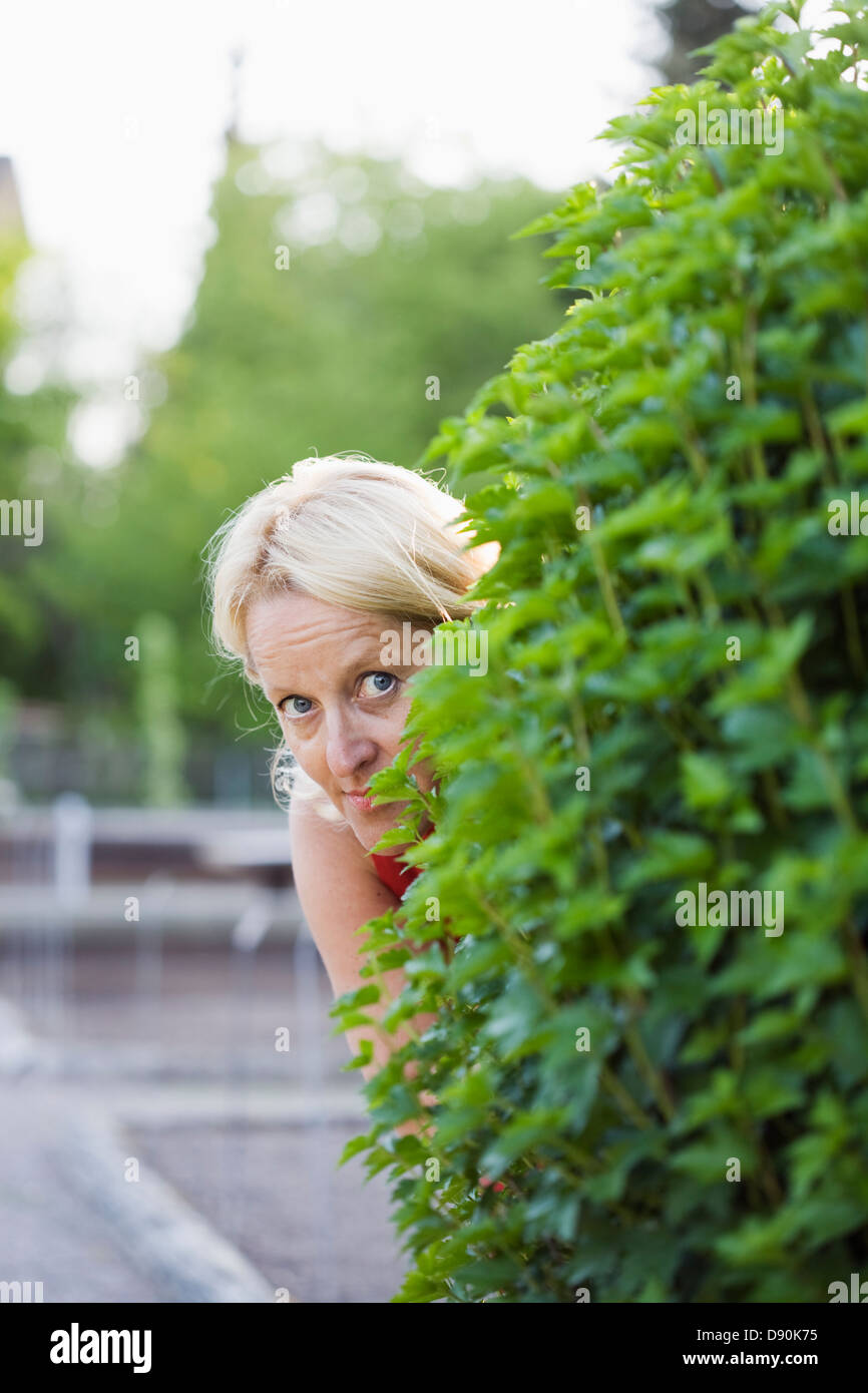 Close-up view of mature woman peeking from behind hedge Stock Photo