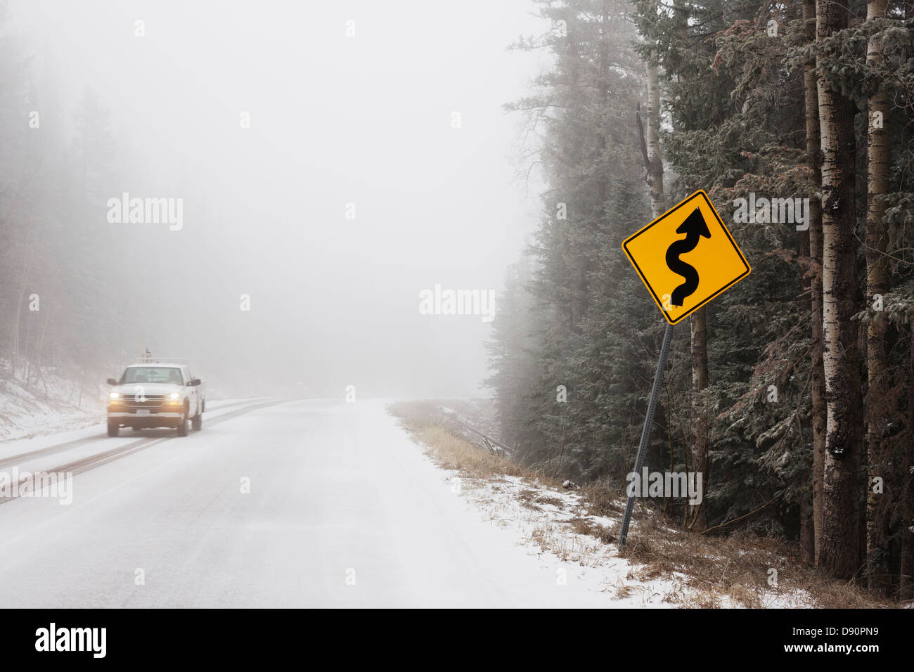 A truck and a curve sign in fog and snow on a mountain road. Stock Photo