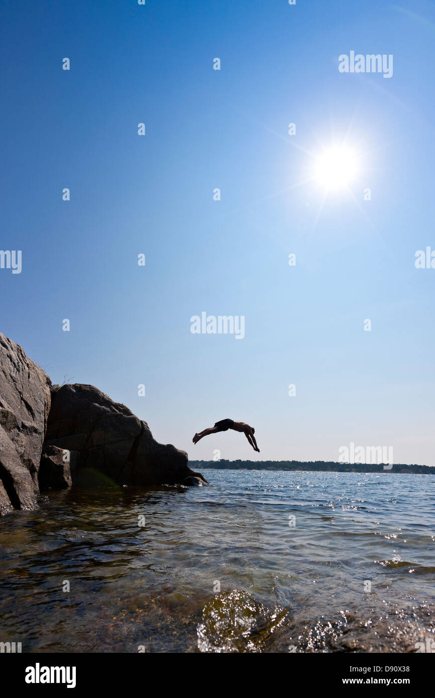 Man jumping from cliff into sea Stock Photo