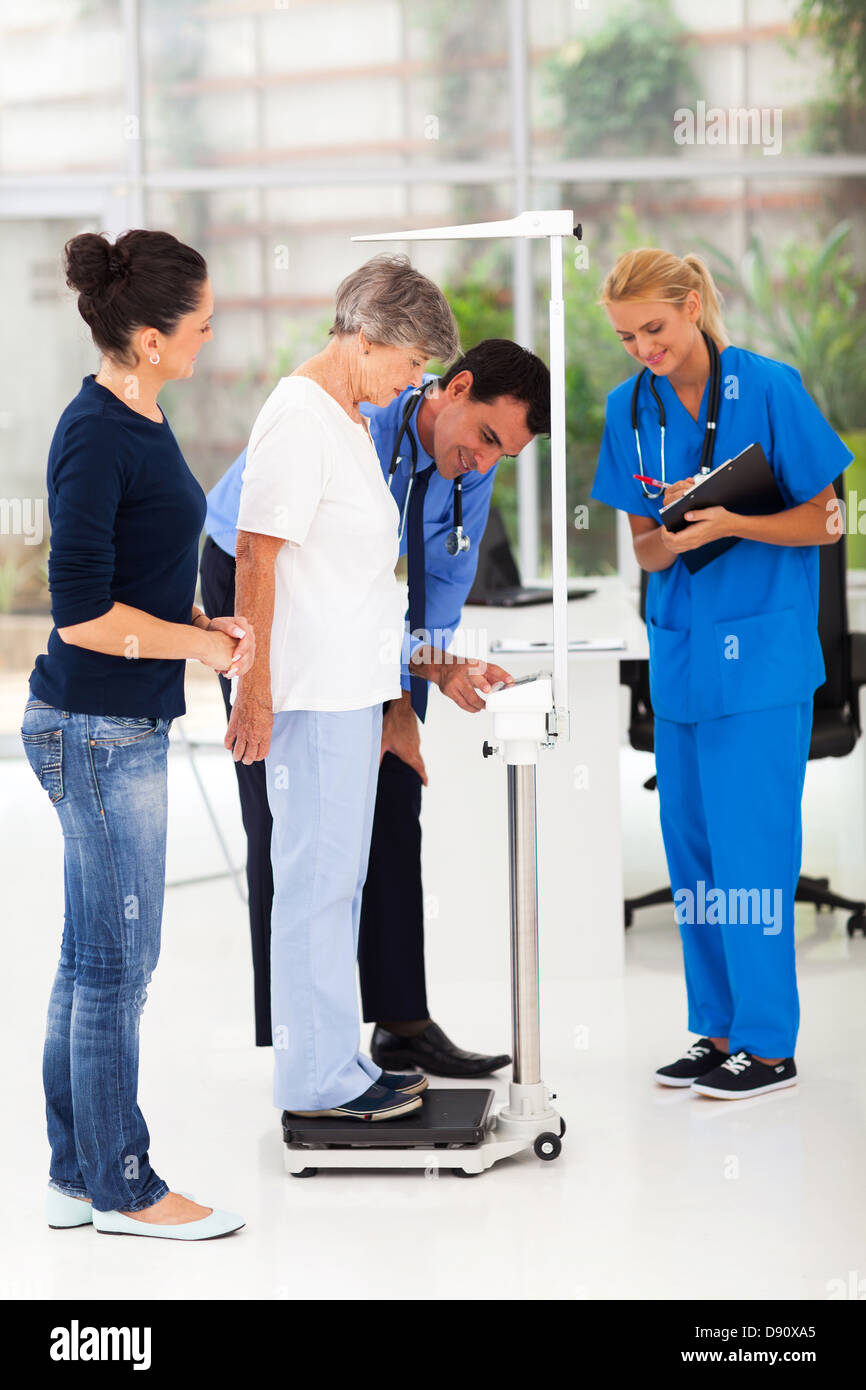 smiling male doctor measuring patient's height and weight on scale Stock Photo